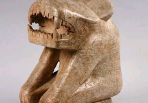 Antropomorficzna postać z głową tygrysa, okrutnym pyskiem. Rzeźba pokryta smokami