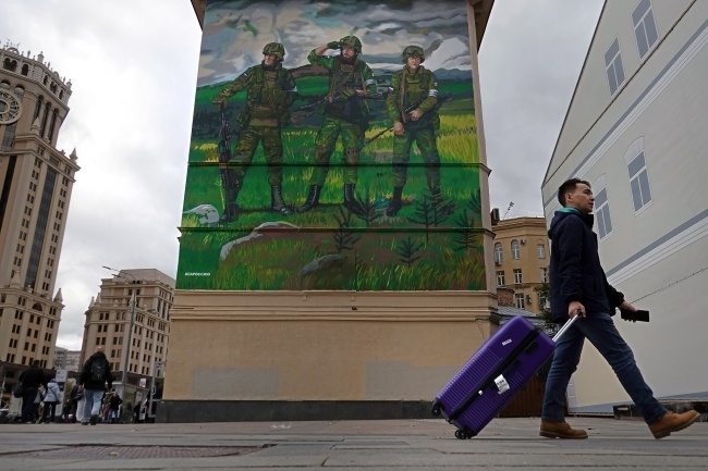 Mężczyzna spaceruje przed blokiem mieszkalnym ozdobionym muralem na poparcie "specjalnej operacji wojskowej" armii rosyjskiej na Ukrainie, w Moskwie, fot. PAP/EPA/MAXIM SHIPENKOV