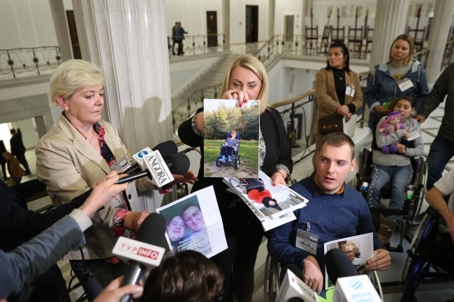 Iwona Hartwich (C) podczas konferencji prasowej z osobami niepełnosprawnymi oraz ich opiekunami na korytarzu Sejmu w Warszawie. Fot. PAP/Rafał Guz
