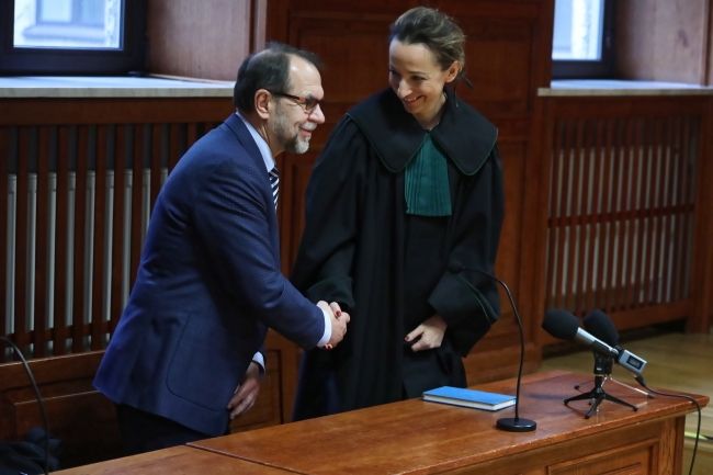 Mężczyzna z brodą ściska dłoń kobiety ubranej w togę adwokacką