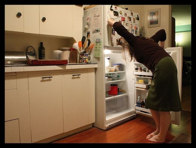 kobieta stoi boso w kuchni i zagląda do lodówki