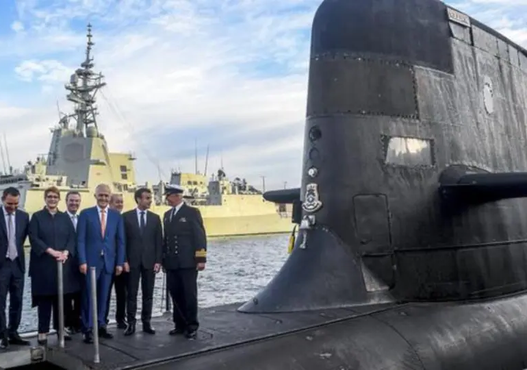 Prezydent Macron, oficer marynarki i 5 innych osób stoi na pokładzie okrętu podwodnego w porcie.