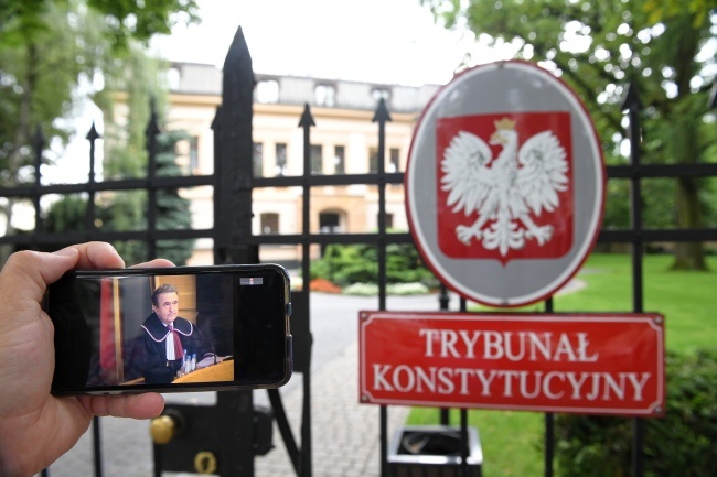 Widziana na wyświetlaczu smartfona relacja z posiedzenia TK, w tle siedziba Trybunału Konstytucyjnego w Warszawie, fot. PAP/Radek Pietruszka