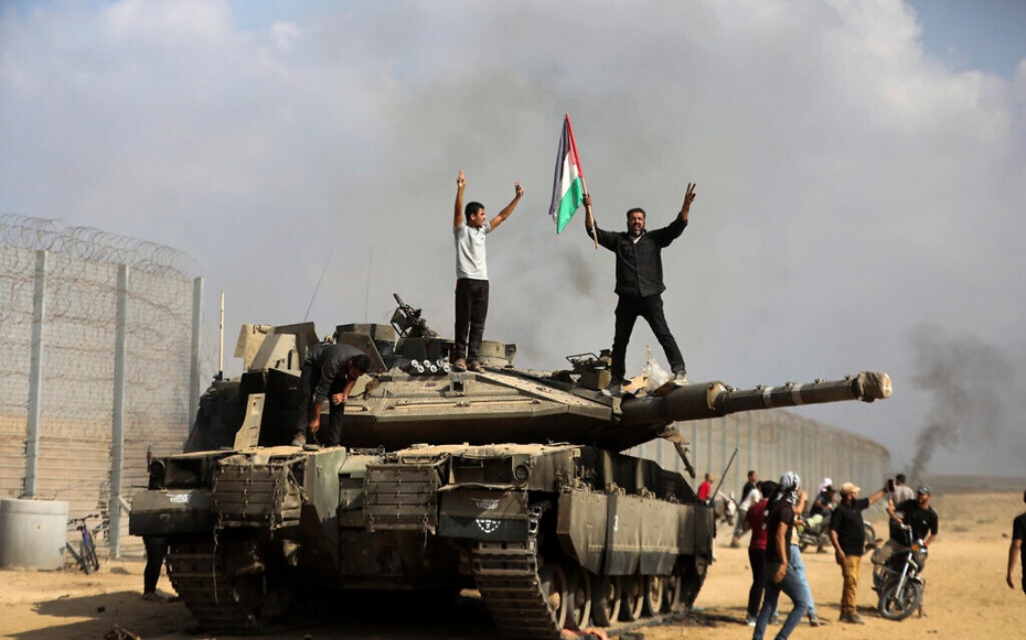 Palestyńczycy machają flagą narodową i świętują przy zniszczonym izraelskim czołgu przy płocie Strefy Gazy na wschód od Khan Younis, 7 października 2023 r. (AP Photo/Yousef Masoud)