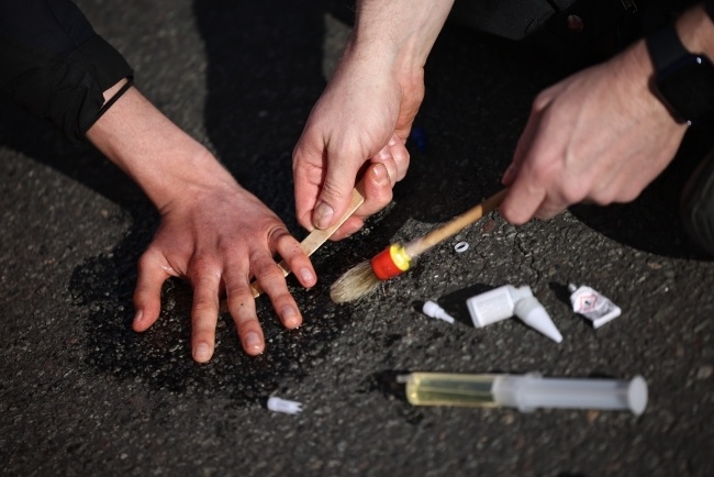 Operacja odklejania ręki aktywisty z asfaltu przez policjanta. Fot.  	PAP/EPA/CLEMENS BILAN