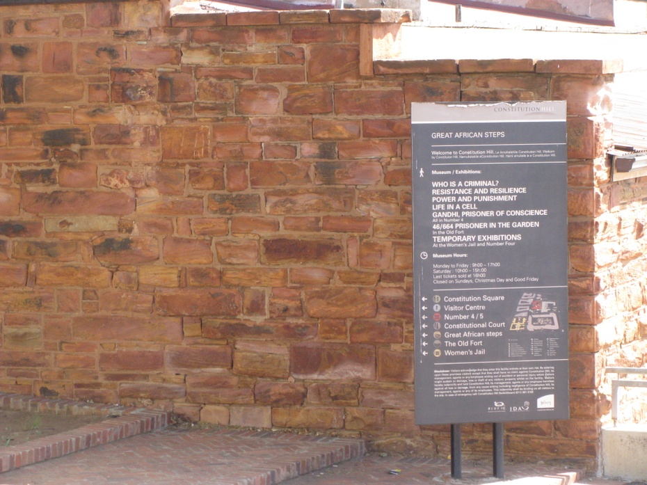 Zdjęcie ilustracyjne przedstawiające tablicę informująca o wystawie dotyczącej systemu penitencjarnego. Constitution Hill, Johannesburg. Wrzesień 2016, zdjęcie własne